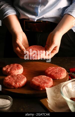 Donna che prepara gustosi cutlet fatti di forcemeat fresco su sfondo scuro, primo piano Foto Stock