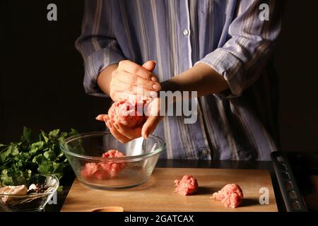 Donna che prepara gustosi cutlet fatti di forcemeat fresco su sfondo scuro, primo piano Foto Stock