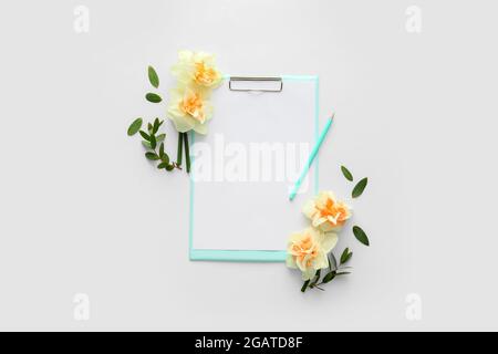Bellissimi narcisi e appunti con foglio di carta bianco su sfondo bianco Foto Stock