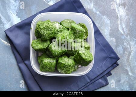 Contenitore con spinaci surgelati su sfondo a colori Foto Stock
