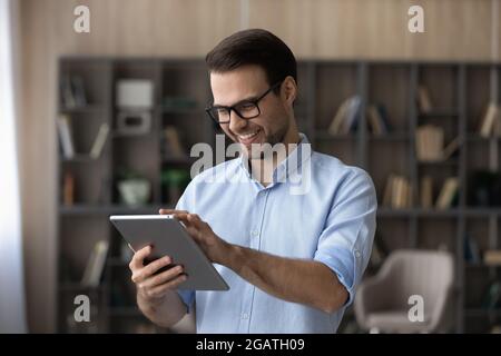 Un giovane sorridente gioca sul tablet pc in salotto Foto Stock