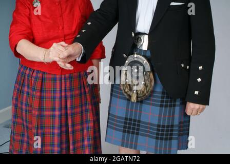 Coppia di Scottish Country Dancing. Indossa un chilt di tartan, una giacca nera e una sporran aggrappata. Indossa una gonna in tartan e una blusa rossa. Tengono le mani Foto Stock