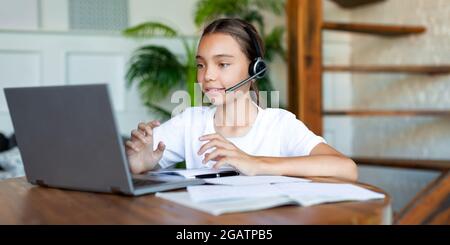 Foto di una ragazza con cuffia durante una lezione online. Si siede di fronte al monitor del computer portatile e fa i suoi compiti online e consulta con il teac Foto Stock