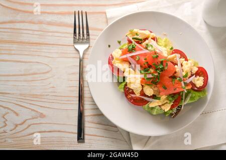 Sandwich con pomodori, uova strapazzate e salmone affumicato su un piatto bianco e un tavolo di legno luminoso con spazio copia, vista dall'alto, selec Foto Stock