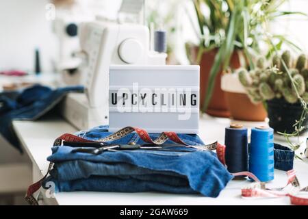 Denim Upcycling Ideas, utilizzando vecchi jeans, riutilizzando jeans, riutilizzando vecchi jeans, Upcycle Stuff. Scatola luminosa con testo Upcycling, pila di vecchi jeans blu Foto Stock