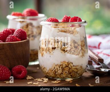 Primo piano di una parfait di granola con yogurt e lamponi freschi su un tavolo di legno Foto Stock