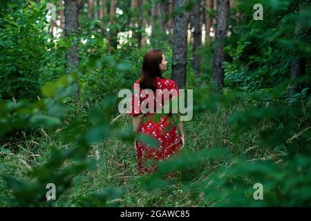 Salvare e piantare alberi, salvare la Terra e la natura, stare per gli alberi, salvare le foreste e guarire il clima. Donna in un vestito rosso che cammina nella foresta, abbracciando gli alberi Foto Stock