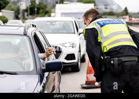 Kiefersfelden, Germania. 01 agosto 2021. Il conducente e il passeggero di un veicolo proveniente dall'Austria mostrano i propri certificati di vaccinazione digitale sui loro smartphone a un ufficiale di polizia federale tedesco al confine con l'Austria sull'autostrada A93. La polizia federale ha iniziato i controlli sui requisiti più rigorosi per i rimpatriati di viaggio. Credit: Attias Balk/dpa/Alamy Live News Foto Stock