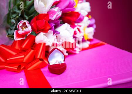 Primo piano foto dell'anello di fidanzamento meraviglioso per la ragazza sulla scatola attuale con il bouquet di tulipani multicolore. Foto Stock