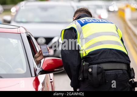 Kiefersfelden, Germania. 01 agosto 2021. Il conducente di un veicolo proveniente dall'Austria mostra i suoi certificati di vaccinazione digitale sui suoi smartphone a un ufficiale di polizia federale tedesco al confine con l'Austria sull'autostrada A93. La polizia federale ha iniziato i controlli sui requisiti più rigorosi per i rimpatriati di viaggio. Credit: Matthias Balk/dpa - ATTENZIONE: Certificato di vaccinazione pixelated for legal reasons/dpa/Alamy Live News Foto Stock