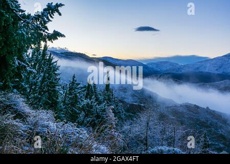Paesaggio montano con alberi in primo piano e nebbia sulle cime dopo una nevicata in Alpujarras. Foto Stock