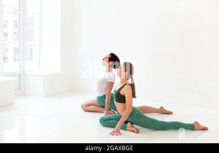 Due giovani donne che fanno yoga indoor, seduti in posizione isolata su sfondo bianco studio. Concetto di sport, yoga e stile di vita sano Foto Stock
