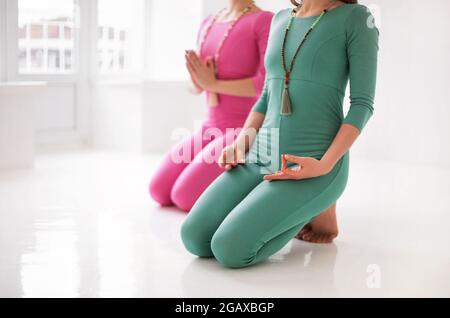 Due giovani donne sane felici in lungo sport Body che eseguono yoga asana insieme durante una formazione abbastanza meditativa o una lezione di yoga di gruppo, isolati Foto Stock