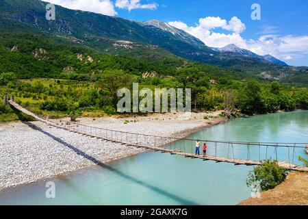 Una madre e un figlio in vacanza attraversando vecchio ponte sospeso sul bellissimo fiume Vjosa, Çarçovë, montagne Nemërçka, Gjirokastra distretto, albania Foto Stock