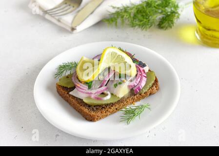 Sandwich con pesce di aringa e cetrioli di sottaceti su piatto bianco Foto Stock