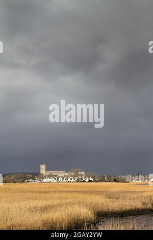 XV secolo Christchurch Priorato iluminato dal Sole contro A Dark Stormy Sky sopra le Reeds Letti di Wick Hengistbury Testa Regno Unito Foto Stock