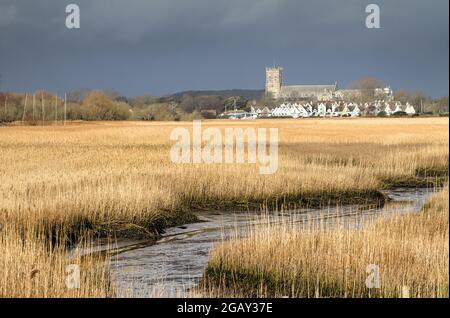 XV secolo Christchurch Priorato iluminato dal Sole contro A Dark Stormy Sky sopra le Reeds Letti di Wick Hengistbury Testa Regno Unito Foto Stock