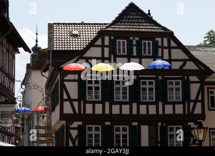 Ombrelli colorati pendono su una corda tra le case sopra la zona pedonale di Bad Kreuznach, Renania-Palatinato, Germania. Foto Stock