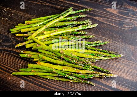 Asparagi arrosto su sfondo di legno scuro: Asparagi arrosto conditi con olio extra vergine di oliva, sale kosher e pepe nero Foto Stock