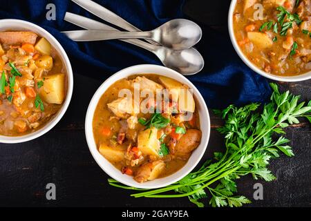 Stufato di pollo con patate e carote in un brodo di vino bianco: Ciotole di pollo fresco condito con prezzemolo tritato Foto Stock