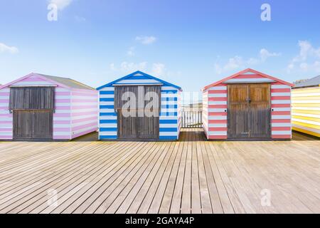 Capanne da spiaggia a strisce di caramelle pastello sul molo di Hastings, East Sussex Foto Stock