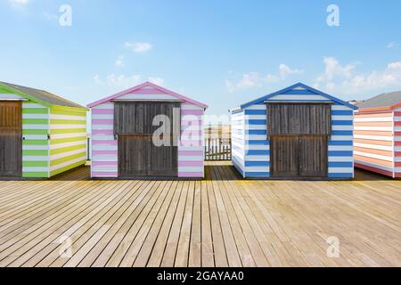 Capanne da spiaggia a strisce di caramelle pastello sul molo di Hastings, East Sussex Foto Stock