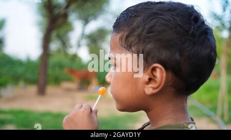 Ragazzino con gelato. Carino ragazzo asiatico mangiare mango bar o caramelle. Isolato su sfondo sfocato Foto Stock