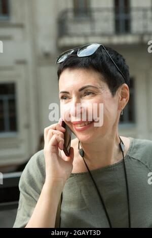 Bella donna di mezza età con un telefono in città. La donna sta parlando emotivamente al telefono. Foto Stock