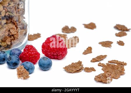 Isolare muesli. I fiocchi di muesli secchi con lamponi e mirtilli si trovano su uno sfondo bianco isolato. Colazione cereali in un vaso di vetro su un bianco Foto Stock