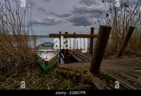 Una piccola barca verde che galleggia sul lago vicino al molo. Foto Stock