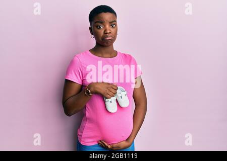 Giovane donna afroamericana che si aspetta un bambino che tiene scarpe depresse e si preoccupa di disagio, piangendo arrabbiato e paura. Triste espressione. Foto Stock