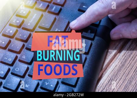 Segno che mostra Fat Burning Foods. Parola scritta su produrre perdita di grasso stimolando il metabolismo per ridurre l'appetito mani che puntano il computer di pressione Foto Stock