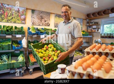 Wiebaden, Germania. 28 luglio 2021. L'agricoltore Ralf Schaab si trova con una cassa di mele appena raccolte nel suo negozio di fattoria a 'Hof Erbenheim', dove offre anche piazzole per campeggiatori. Più di 1,100 ospiti rurali provenienti da tutta la Germania sono elencati nella guida del campeggio 'Landvergnügen', che è venduto insieme alla vignetta annuale. Credit: Frank Rumpenhorst/dpa/Frank Rumpenhorst/dpa/Alamy Live News Foto Stock