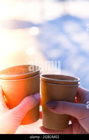 Mano di donne con tazza di carta di caffè in fondo neve invernale. Tazze monouso in carta marrone scuro. Caffè da portare via. Pausa caffè Foto Stock