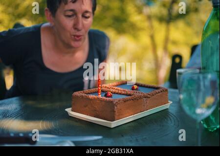 Donna anziana che soffia la candela sulla torta di compleanno Foto Stock