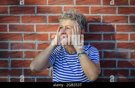 Donna anziana in piedi all'aperto contro muro di mattoni sfondo, rilassante. Foto Stock