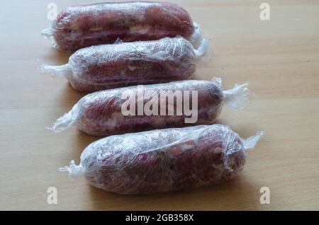 Preparazione graduale del prosciutto tagliato in casa. Fase 13: Quattro rotoli di prosciutto crudo avvolti in pellicola di rivestimento e legati con filo. Pronto per l'ulteriore cottura Foto Stock