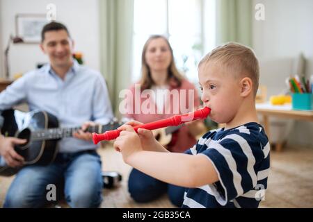 Allegro ragazzo sindrome giù con i genitori che suonano strumenti musicali, ridendo. Foto Stock