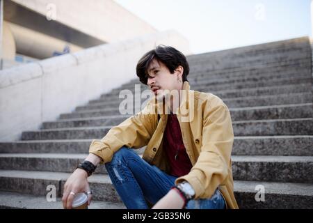 Ritratto di triste giovane seduto su scala all'aperto in città, riposante. Foto Stock