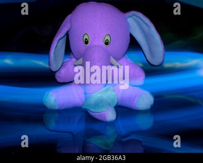 Elefante morbido giocattolo isolato con sfondo bluastro effetto luce. Foto Stock