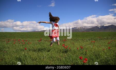 Felice ragazza di saltare sul campo di tulipani contro Sky Foto Stock