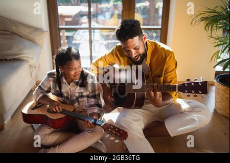 Vista ad alto angolo del padre felice con la piccola figlia al chiuso a casa, suonando la chitarra. Foto Stock