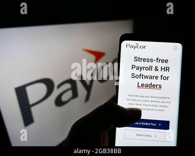 Persona che detiene il telefono cellulare con la pagina web della società di software HR USA Paycor HCM Inc. Sullo schermo davanti al logo. Mettere a fuoco il centro del display del telefono. Foto Stock