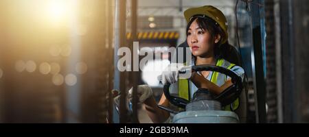 Asian bella donna conducente guida carrello elevatore a forcella in industria con sorridente, abilità di ragazza e la diversità di carriera indossare casco in gilet riflettente WO Foto Stock