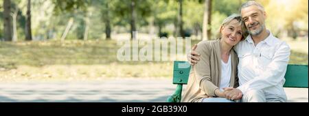 Felice coppia anziana seduta su una panchina di legno nel parco e abbraccio, vecchi genitori usano il tempo insieme in giardino in vacanza, amore e concetto romantico Foto Stock