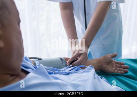 Primo piano mano del medico che lavora e regolare il manometro della pressione sanguigna sulla mano dell'uomo anziano in ospedale Foto Stock