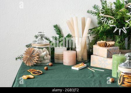 Tavolo festoso decorato Natale o Capodanno, rami thuja e abete rosso, candele e biscotti in un vaso, scatole da regalo e decorazioni di carta Foto Stock