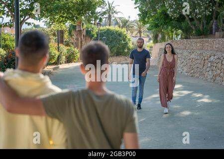 Amici in attesa dei loro amici di arrivare. Stanno arrivando. Indossano colorati abiti estivi. Sono caucasici. Stanno camminando verso Foto Stock
