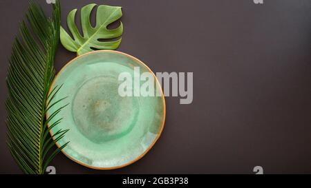 Piastra verde vuota su sfondo nero. Piatto da cena di lusso servito con foglie tropicali di palma monstera in stile kinfolk asiatico. Fock up vuoto Foto Stock