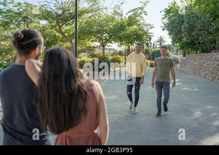 Amici in attesa dei loro amici di arrivare. Stanno arrivando. Indossano colorati abiti estivi. Sono caucasici. Stanno camminando verso Foto Stock